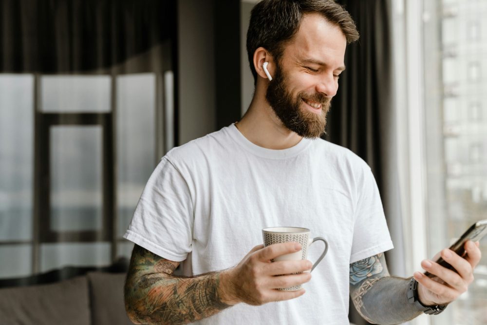 Man wearing earbud smiling while looking at phone.